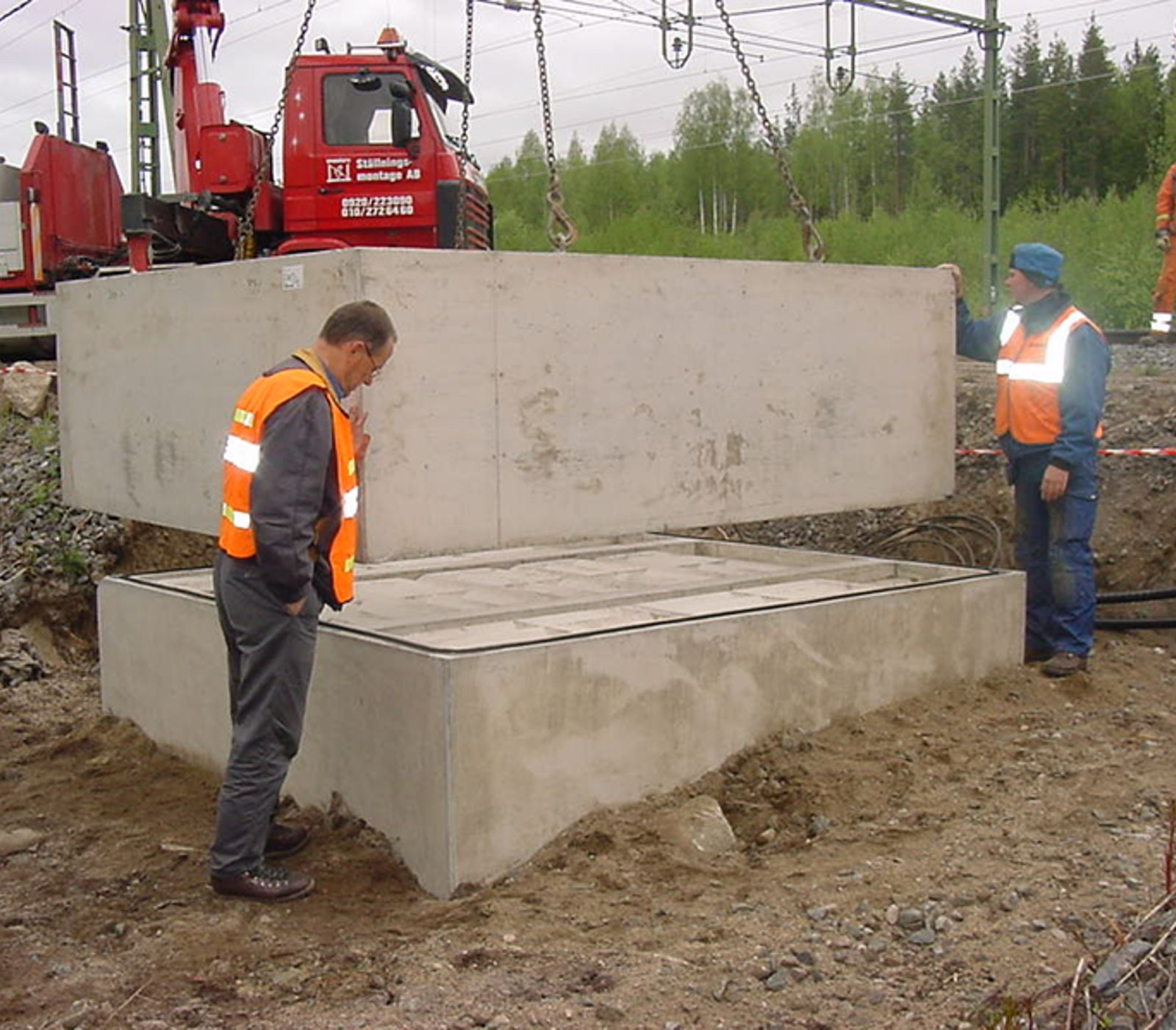 Prefabrikert oljegruve løftes på plass på fundament ved sporområde.