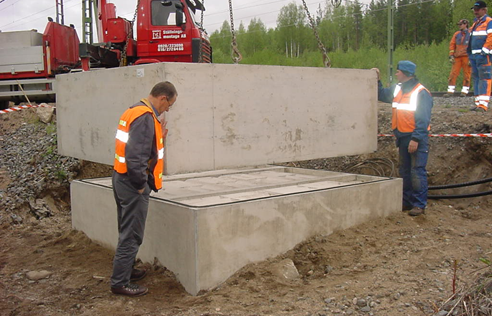Prefabrikert oljegruve løftes på plass på fundament ved sporområde.