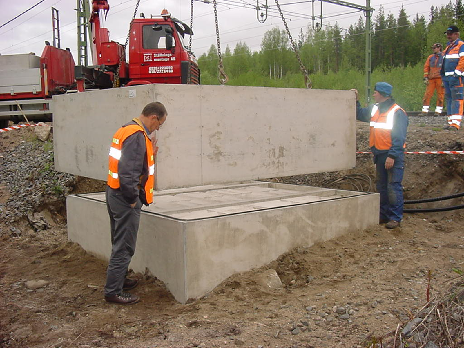 Prefabrikert oljegruve løftes på plass på fundament ved sporområde.