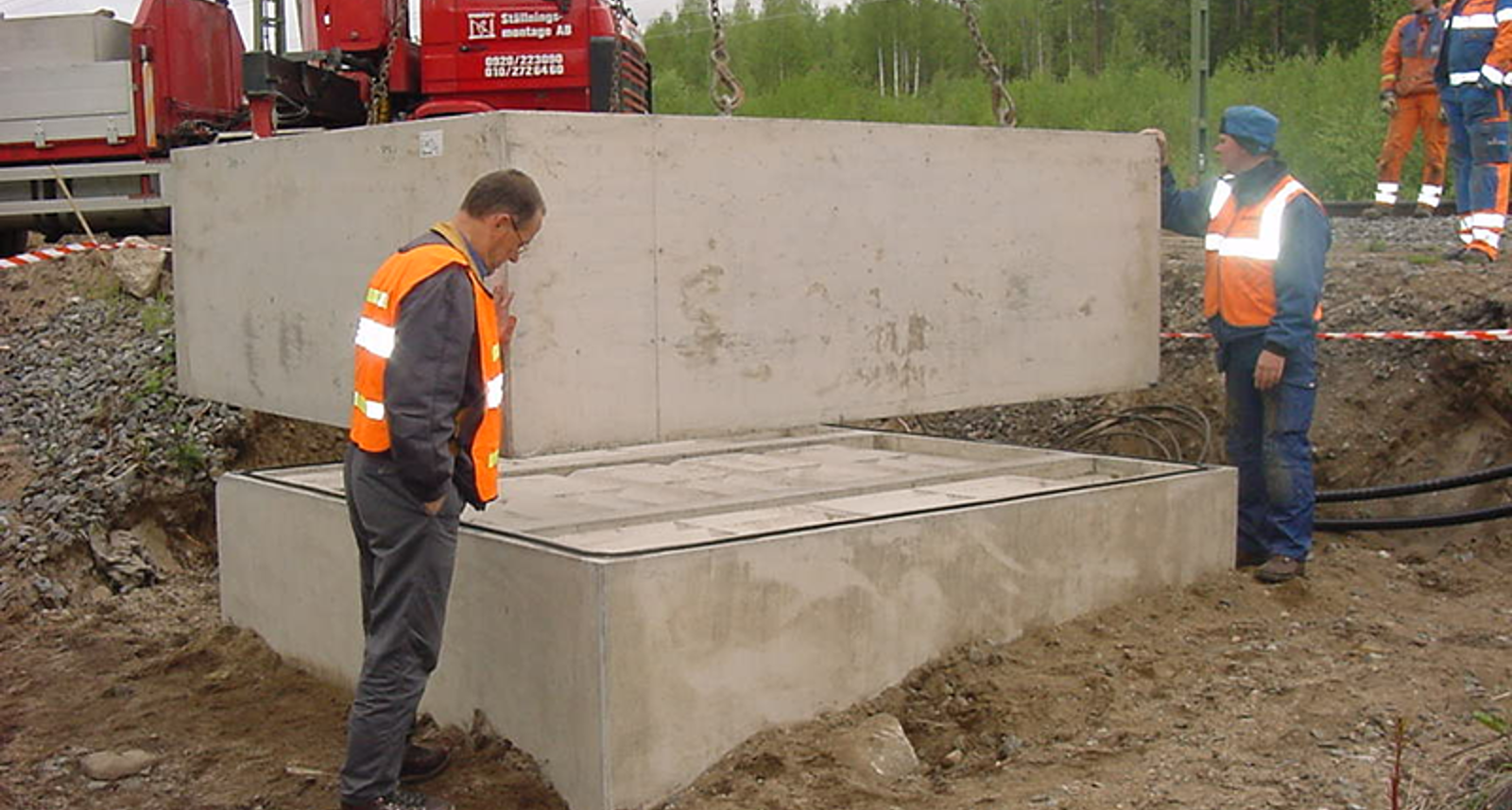 Prefabrikert oljegruve løftes på plass på fundament ved sporområde.