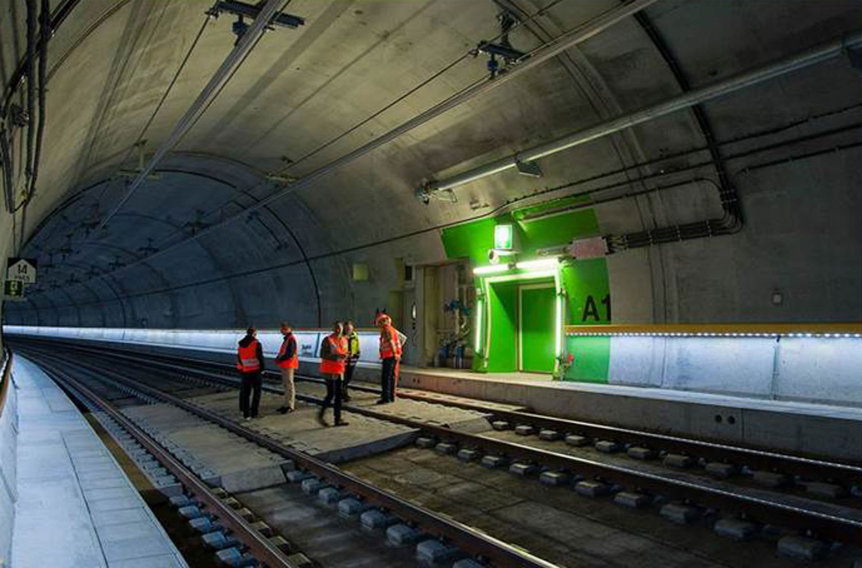 Grønn dør med grønt område rundt, nødutgansskilt og lys, i tunnel