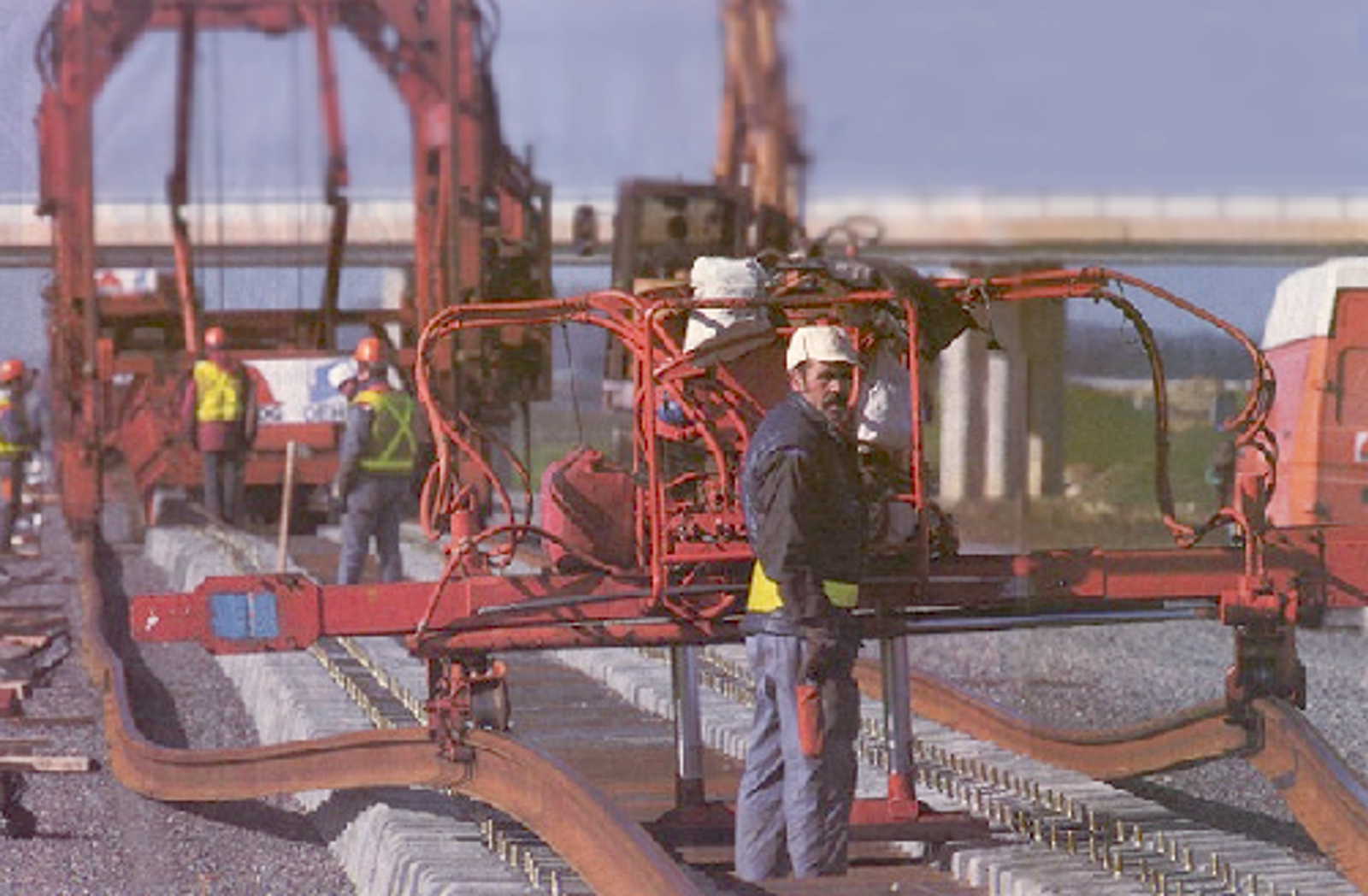 Arbeidere og maskiner legger skinner på plass på svillene ved sporbygging.