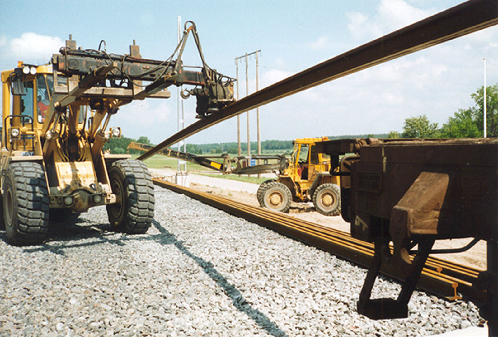 Nærbilde av hjullaster med hydraulisk arm for plassering av jernbaneskinner.
