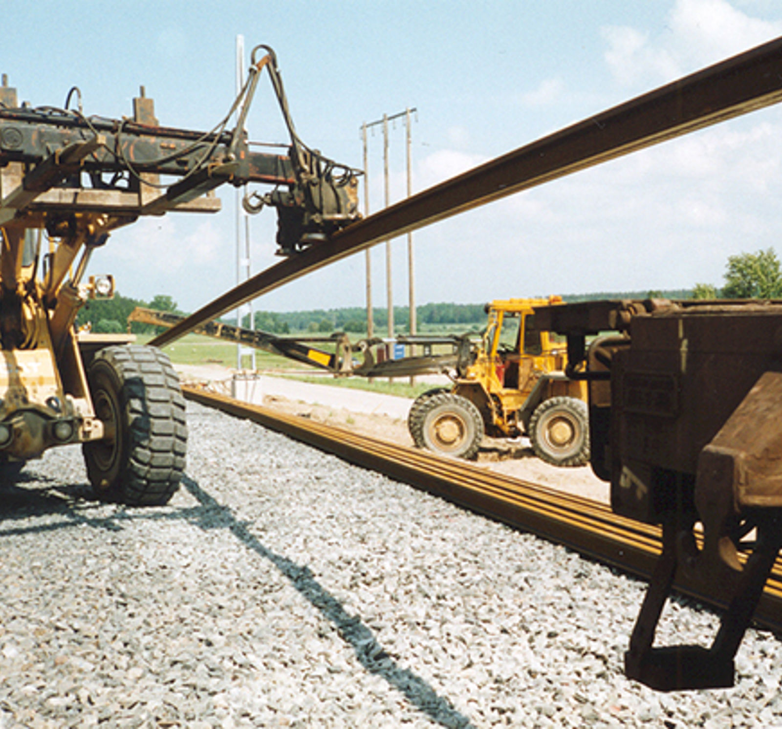 Nærbilde av hjullaster med hydraulisk arm for plassering av jernbaneskinner.