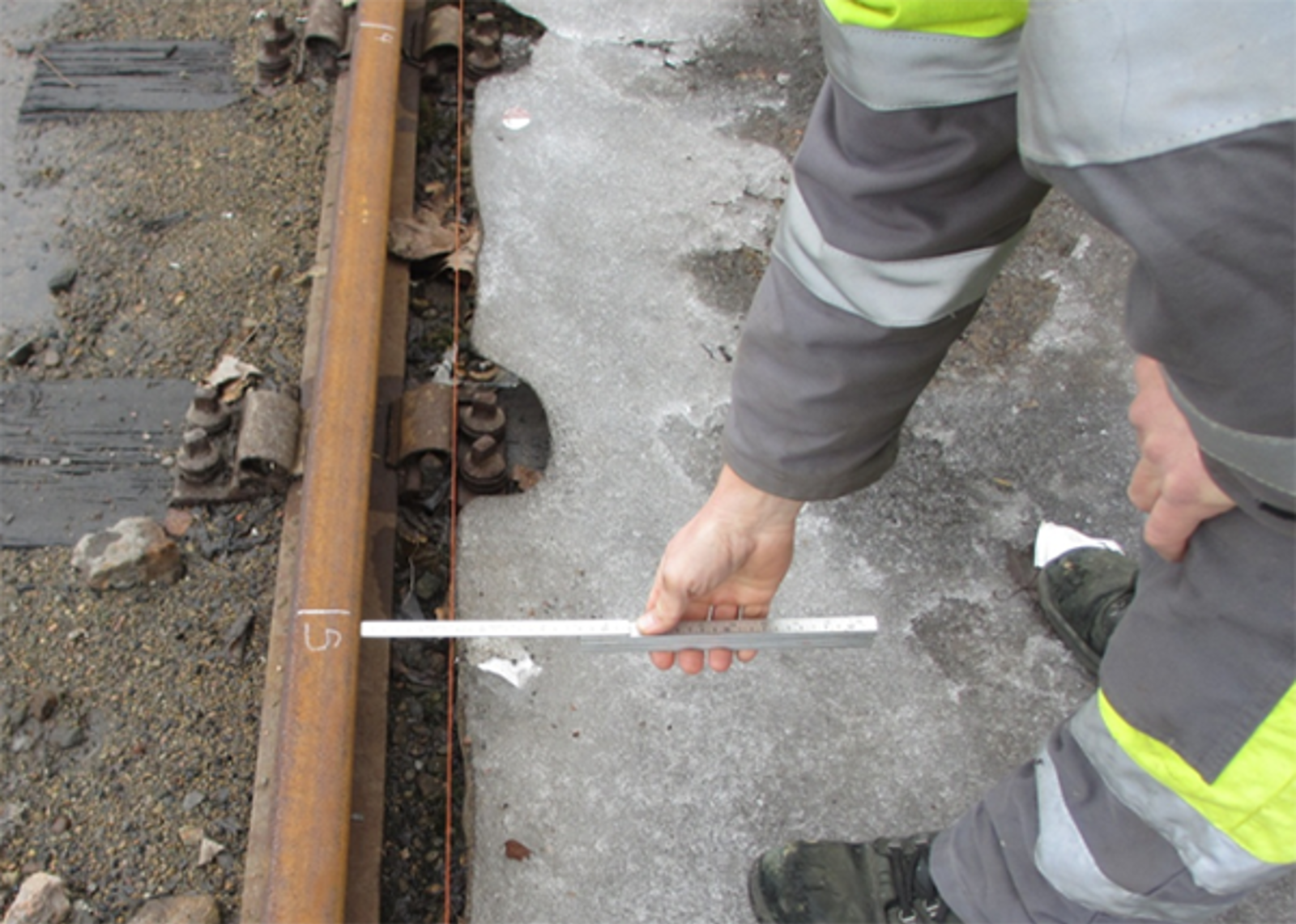 Person måler pilhøyde på skinne med målestav midt under strukket snor for å bestemme sidefeil.