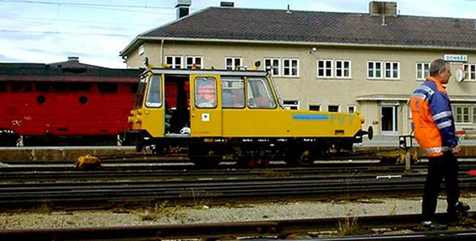 Gul Matisa PV 7-målevogn står på spor ved en stasjon, med en person i refleks foran.