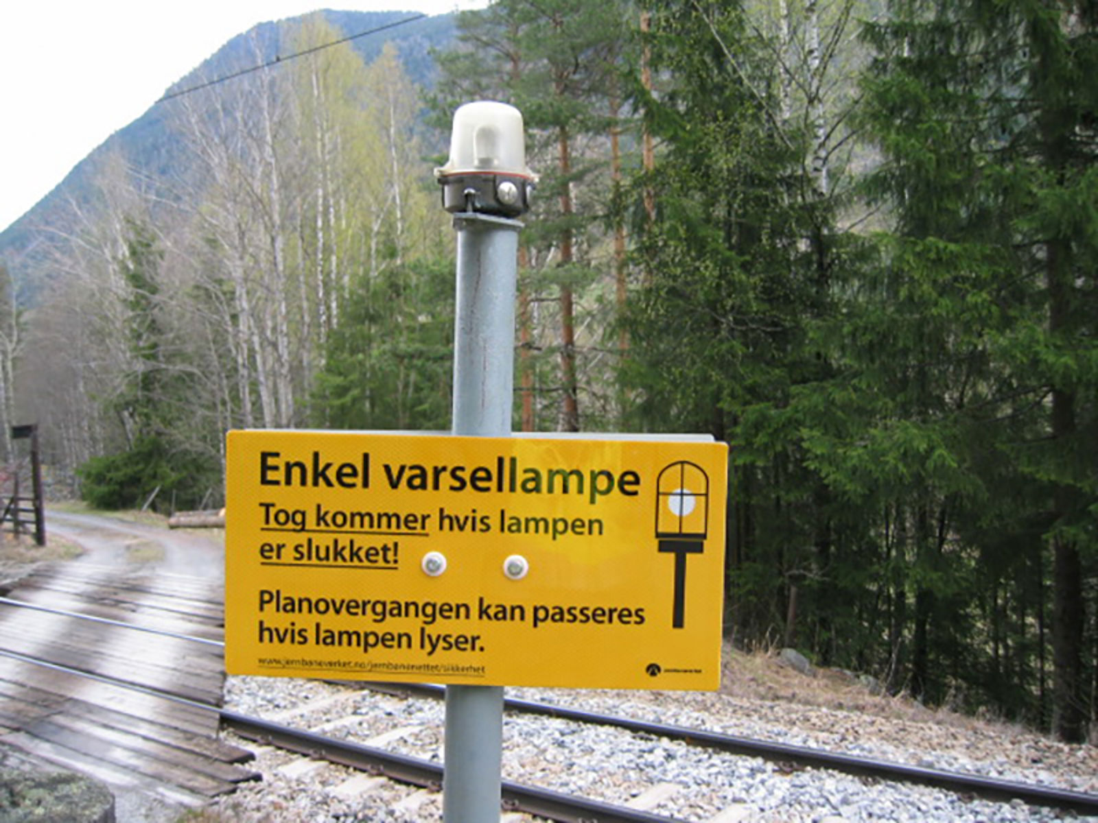 Informasjonsskilt om varsellampe ved planovergang: Tog kommer hvis lampen er slukket.