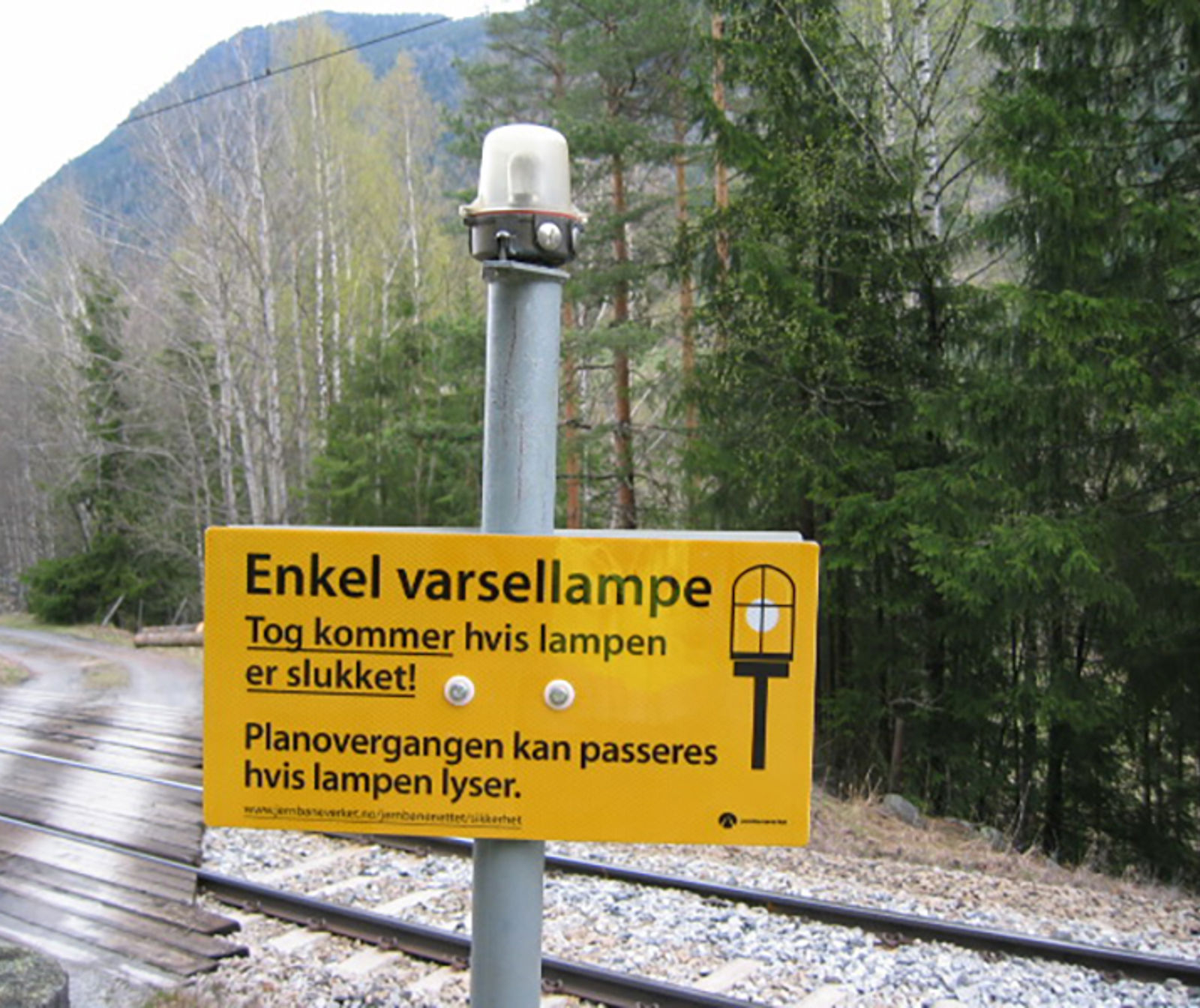 Informasjonsskilt om varsellampe ved planovergang: Tog kommer hvis lampen er slukket.