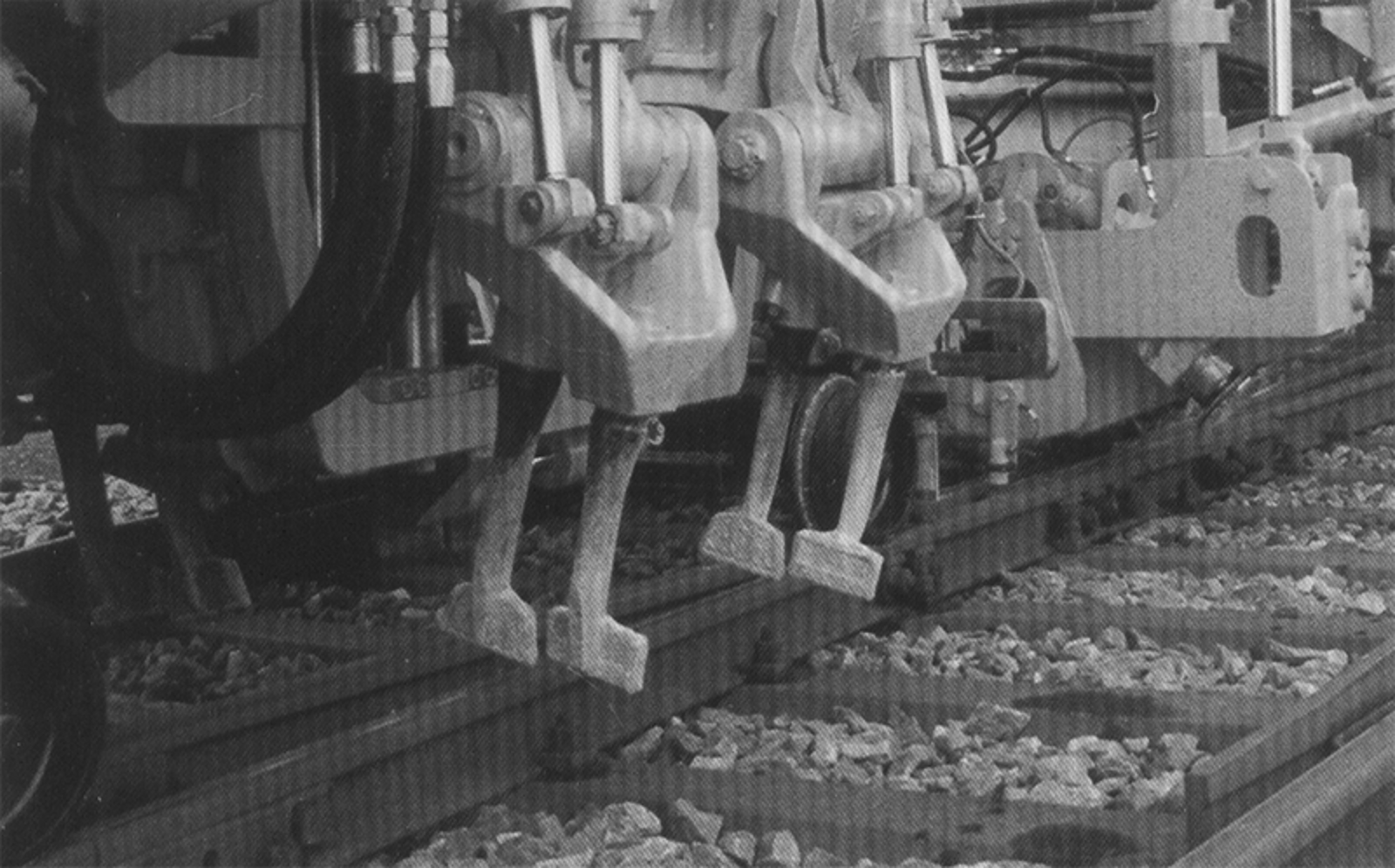 Nærbilde av labbene på en pakkmaskin som føres ned i ballasten for å justere sporet.