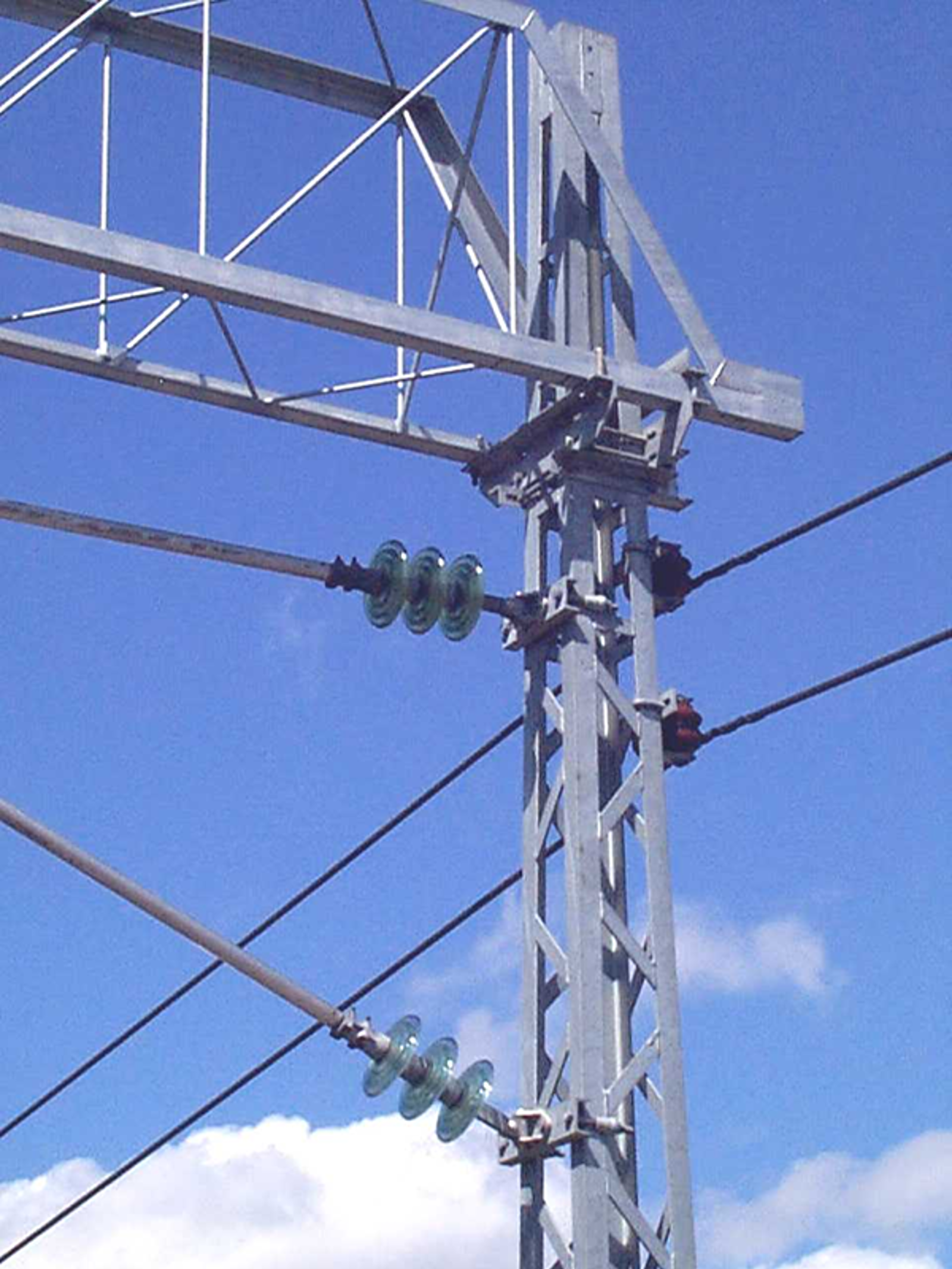 To returledninger montert på mast med isolatorer, symmetrisk plassert bak øvre utliggerkonsoll.