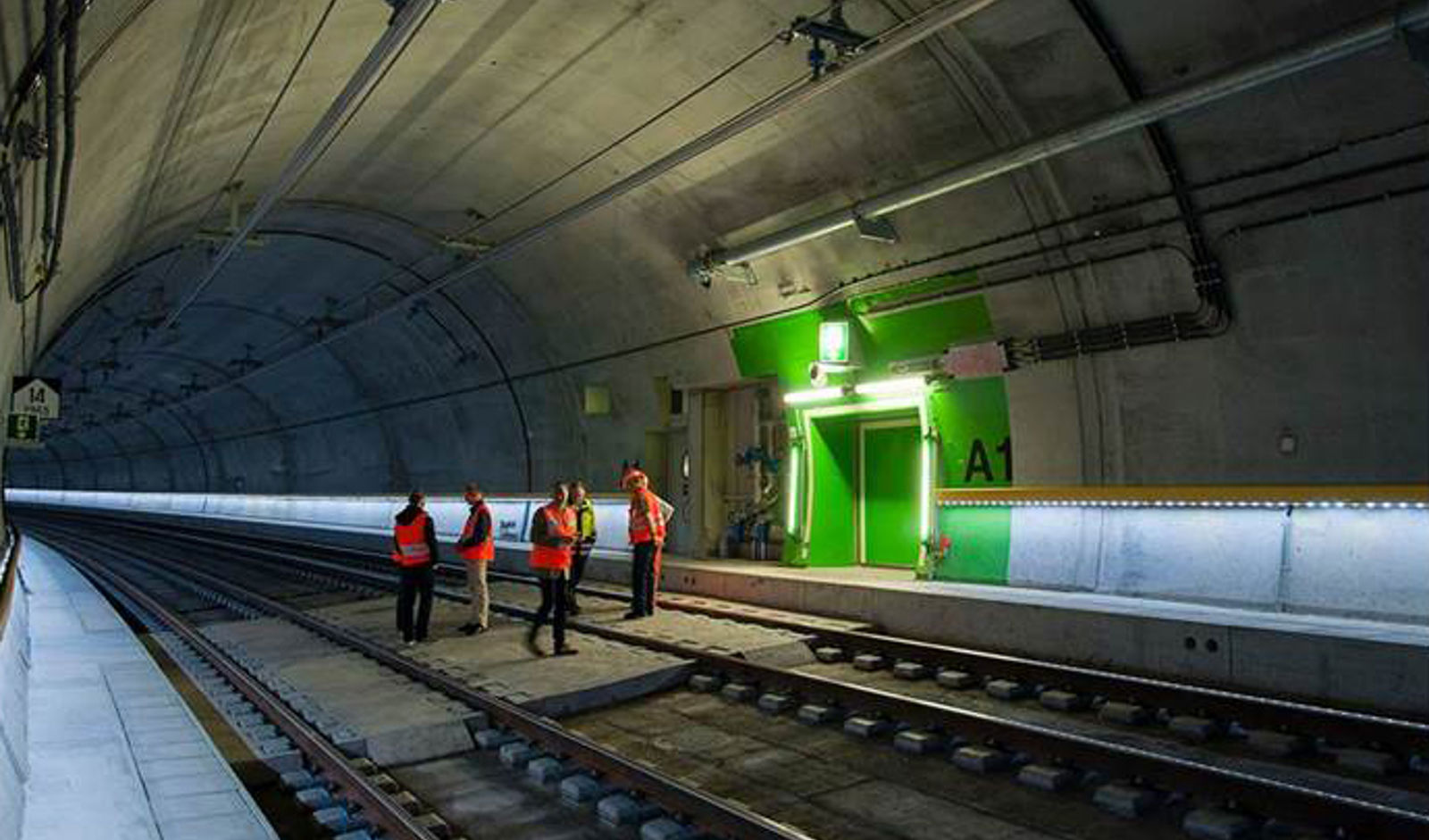 Grønn dør med grønt område rundt, nødutgansskilt og lys, i tunnel