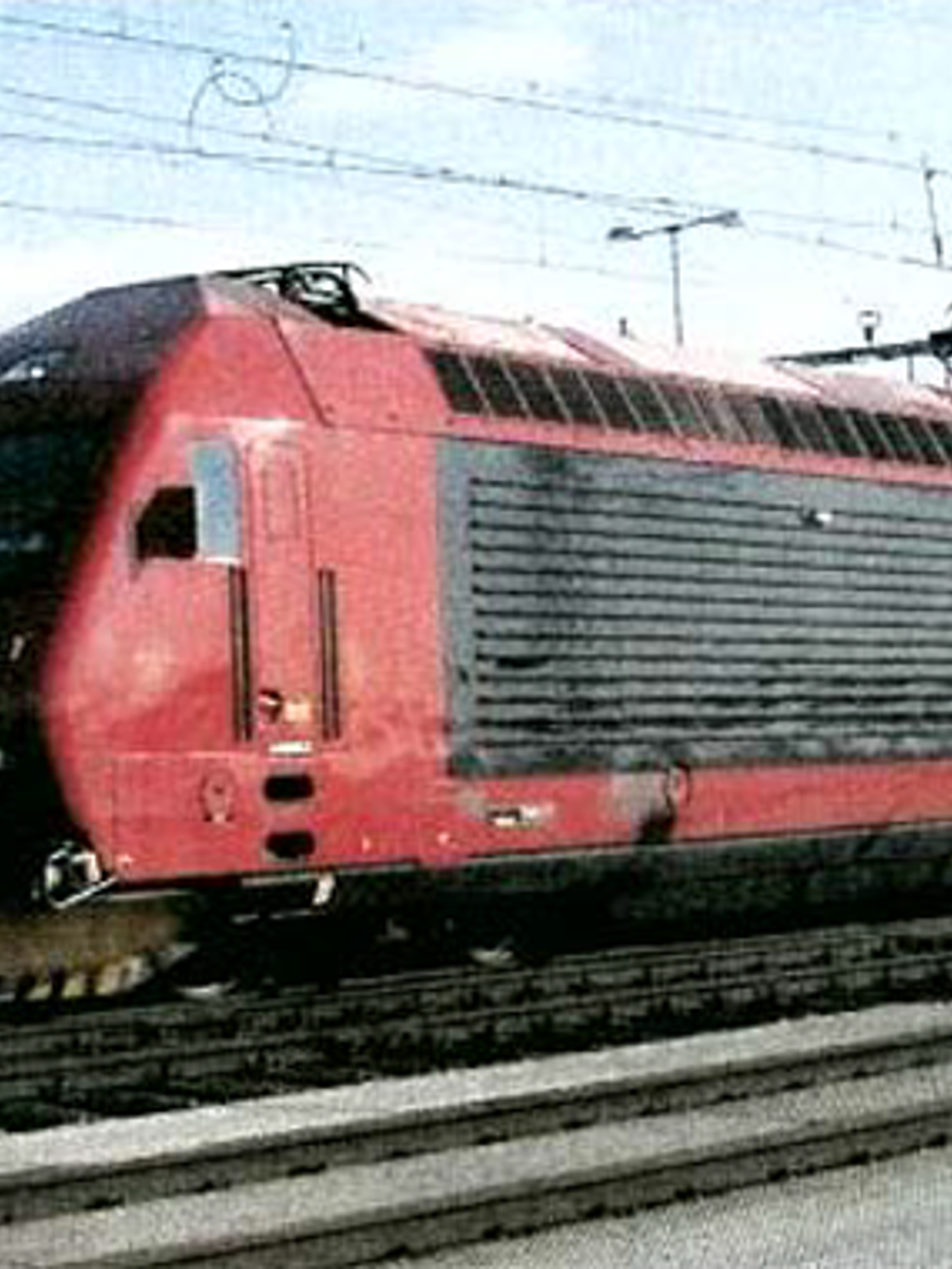 Rødt El 18-lokomotiv på jernbanespor med kjøreledninger i bakgrunnen.