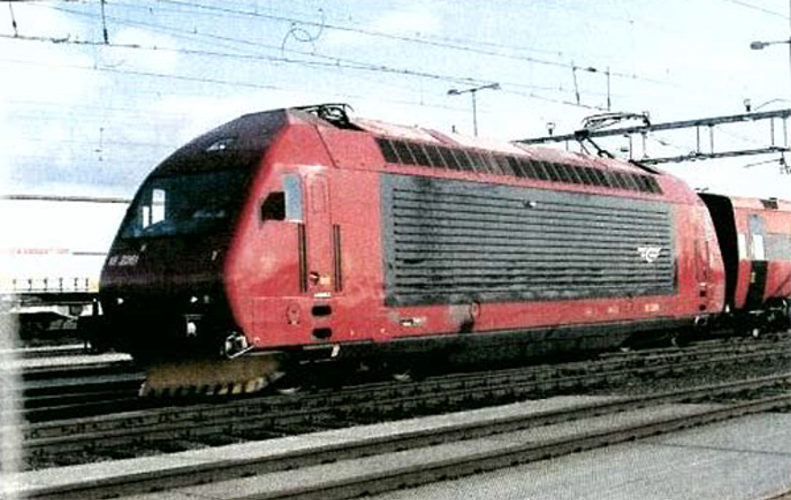 Rødt El 18-lokomotiv på jernbanespor med kjøreledninger i bakgrunnen.