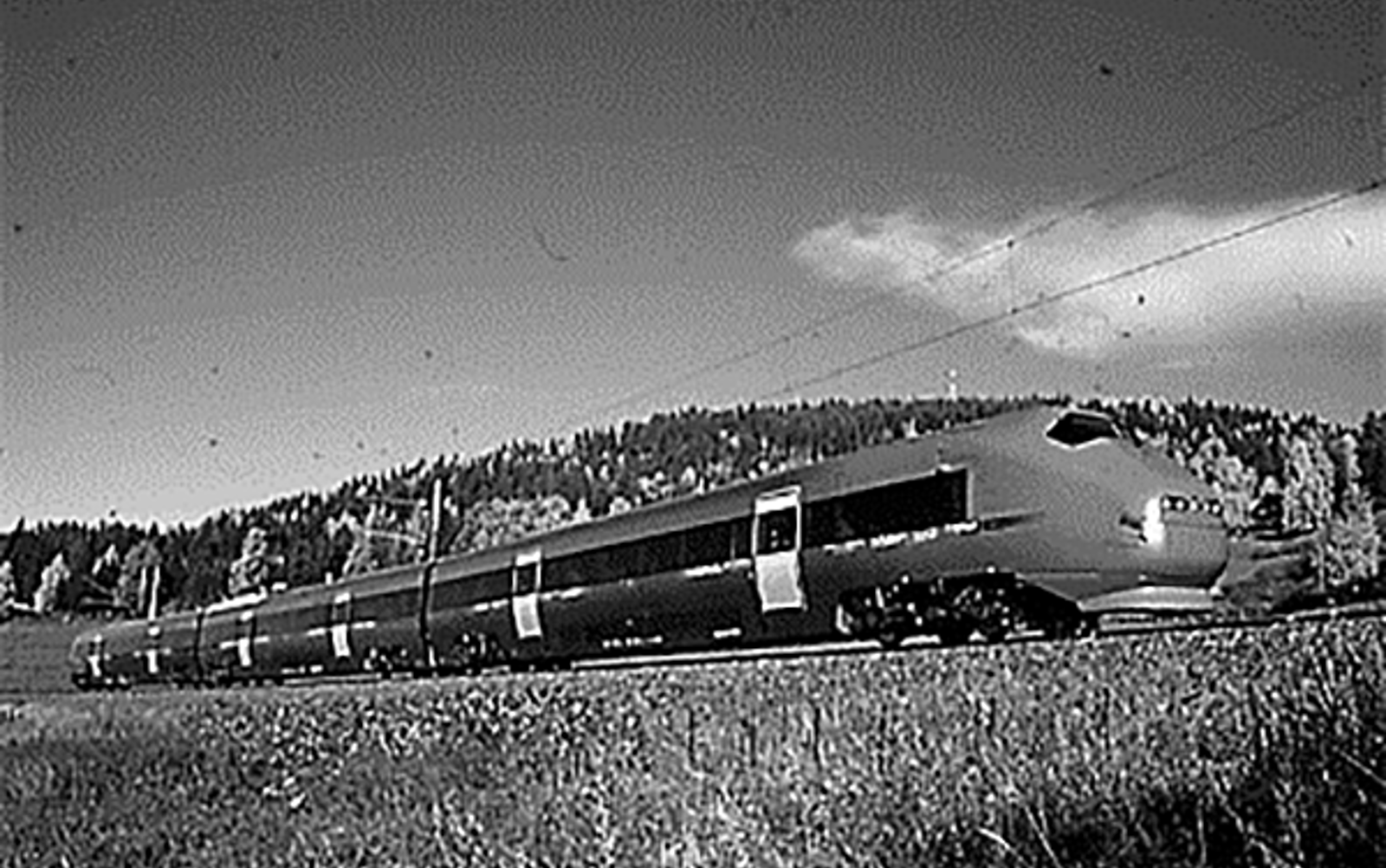 Flytoget type BM71 på høyhastighetsbane i kupert landskap med skog i bakgrunnen.