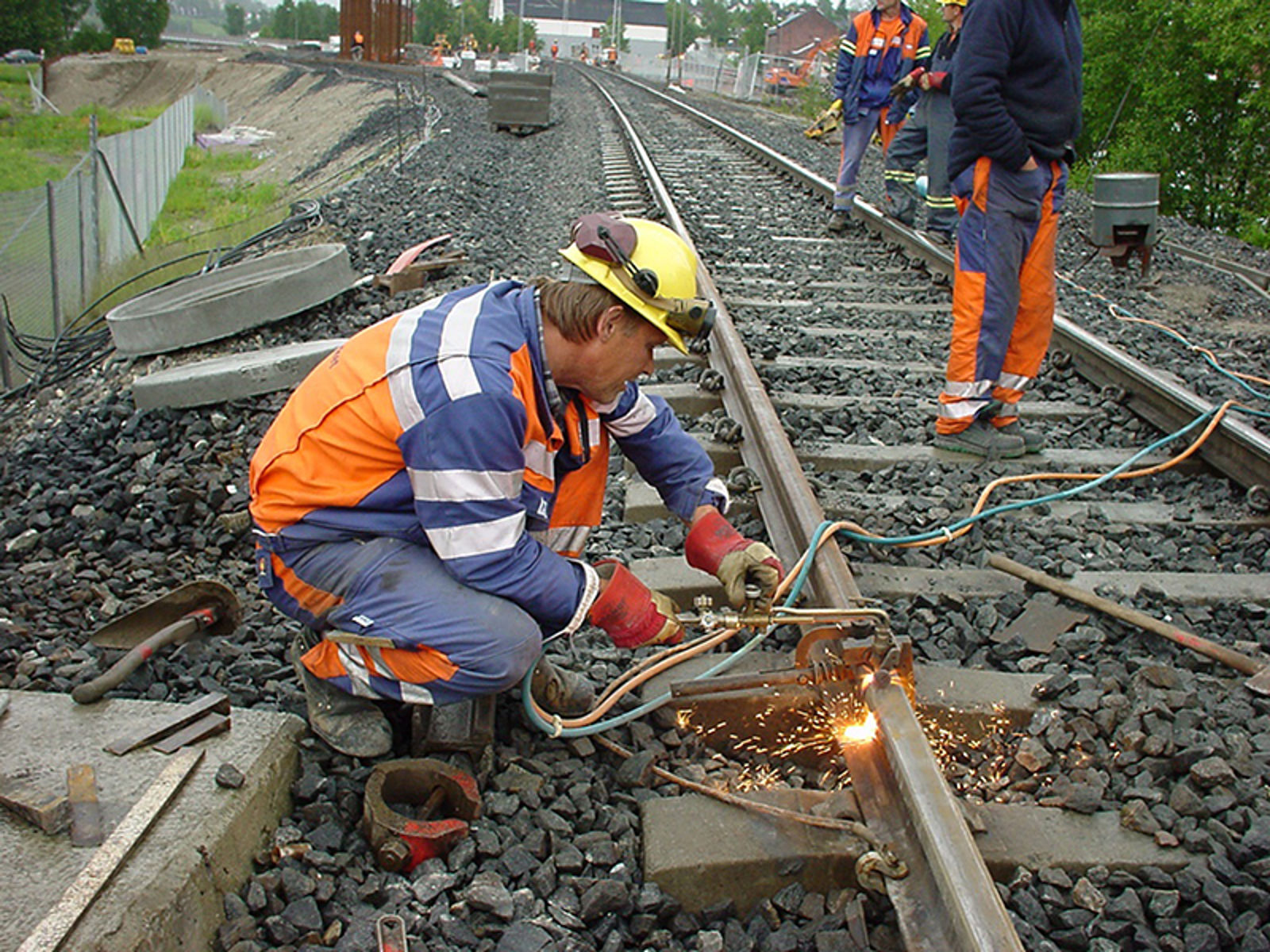 Arbeider skjærebrenner en jernbaneskinne med propan/oksygen-brenner, gnister spruter.