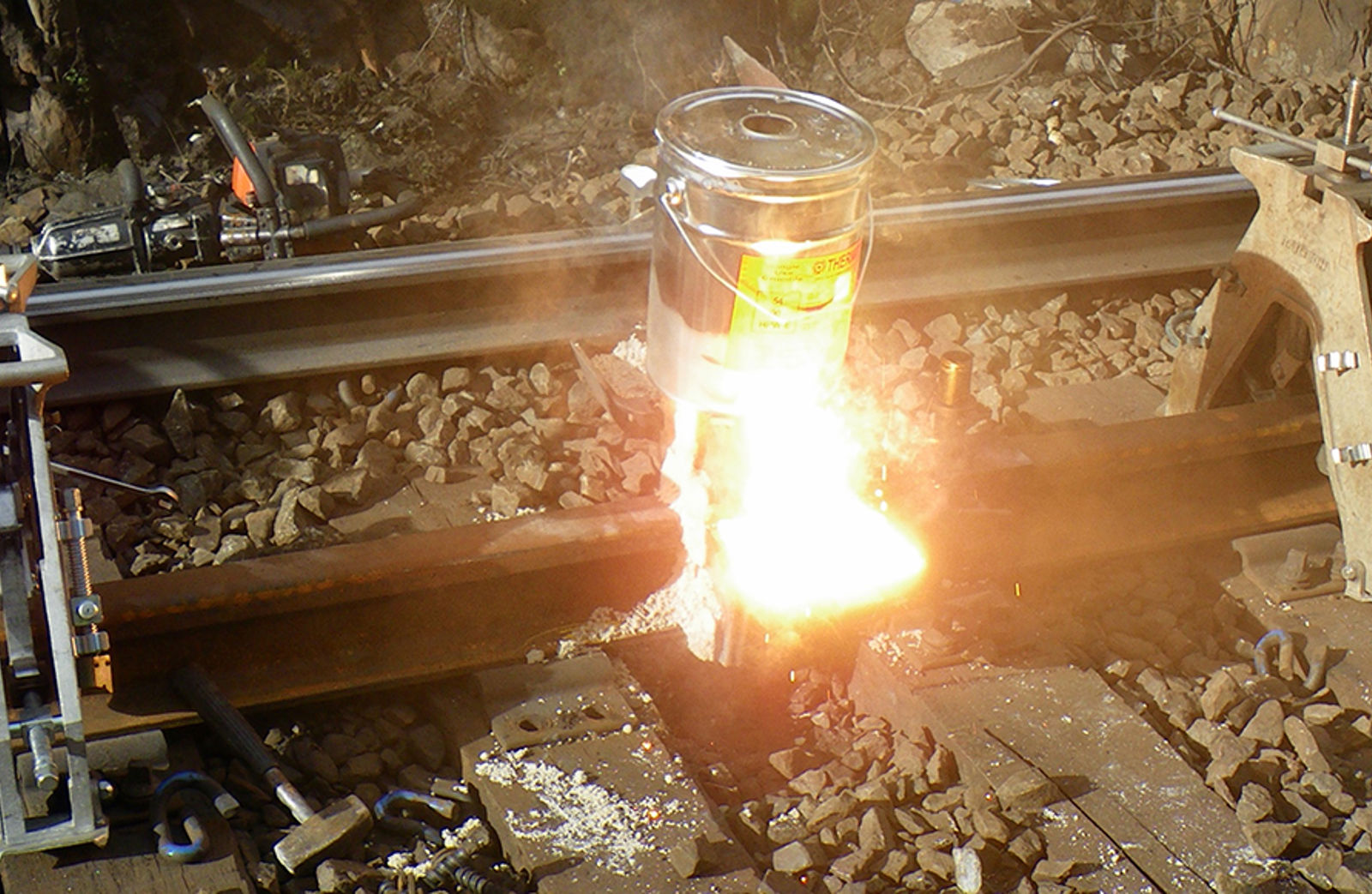 Flytende stål og slagg tappes fra digelen under aluminiotermisk sveising av jernbaneskinner.