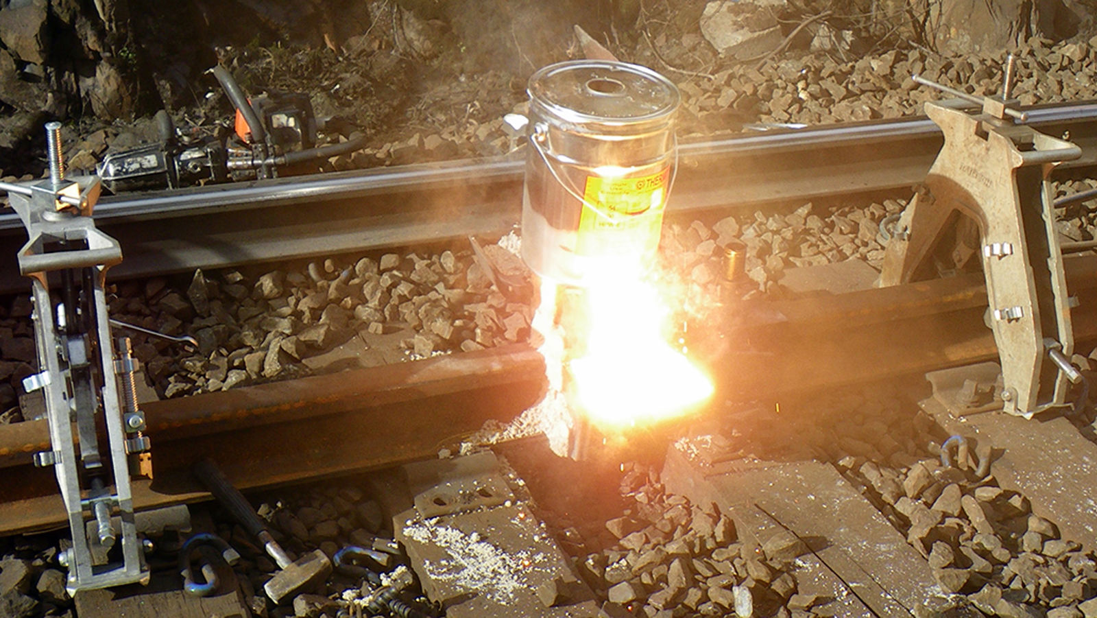 Flytende stål og slagg tappes fra digelen under aluminiotermisk sveising av jernbaneskinner.