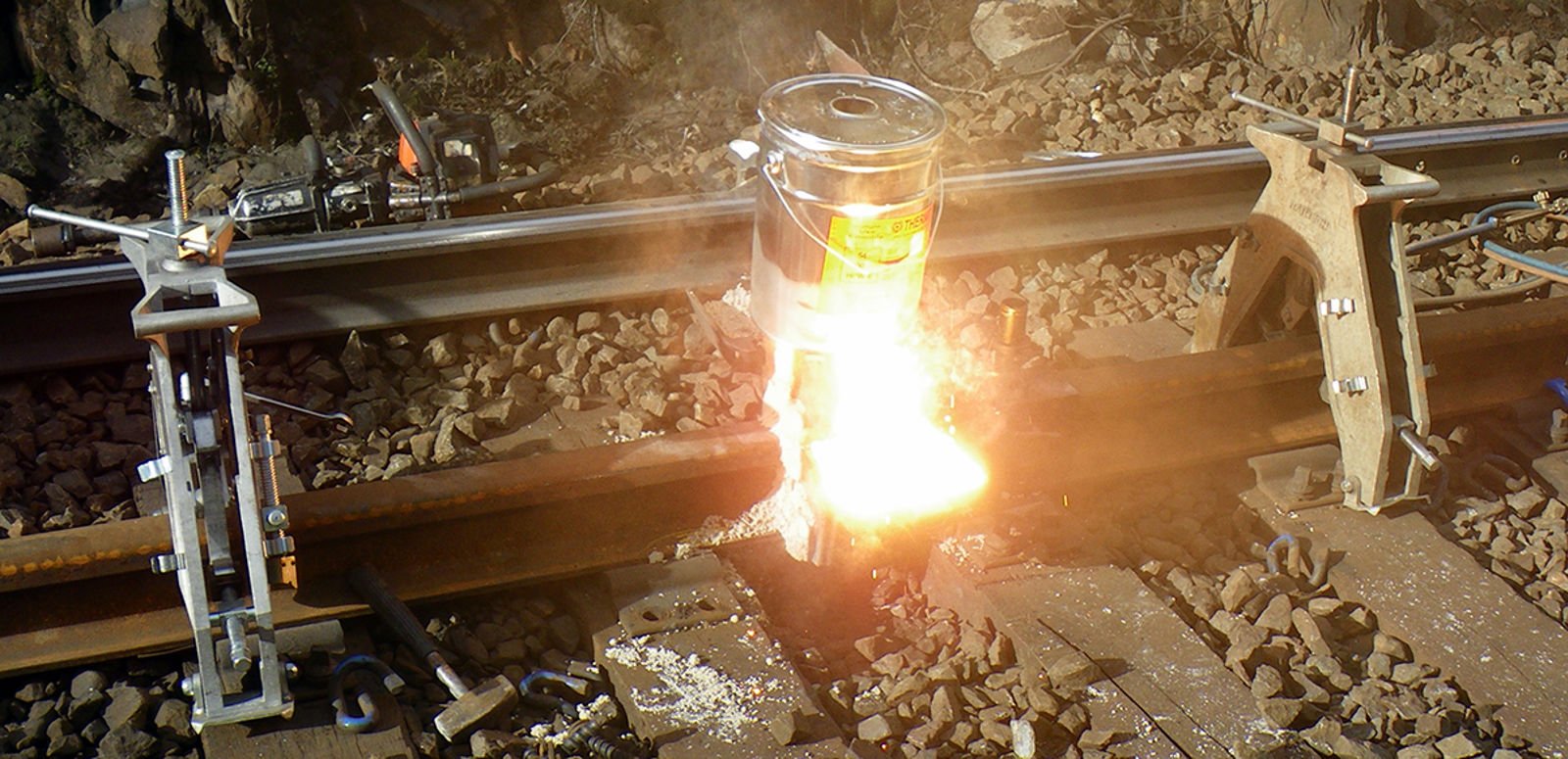 Flytende stål og slagg tappes fra digelen under aluminiotermisk sveising av jernbaneskinner.