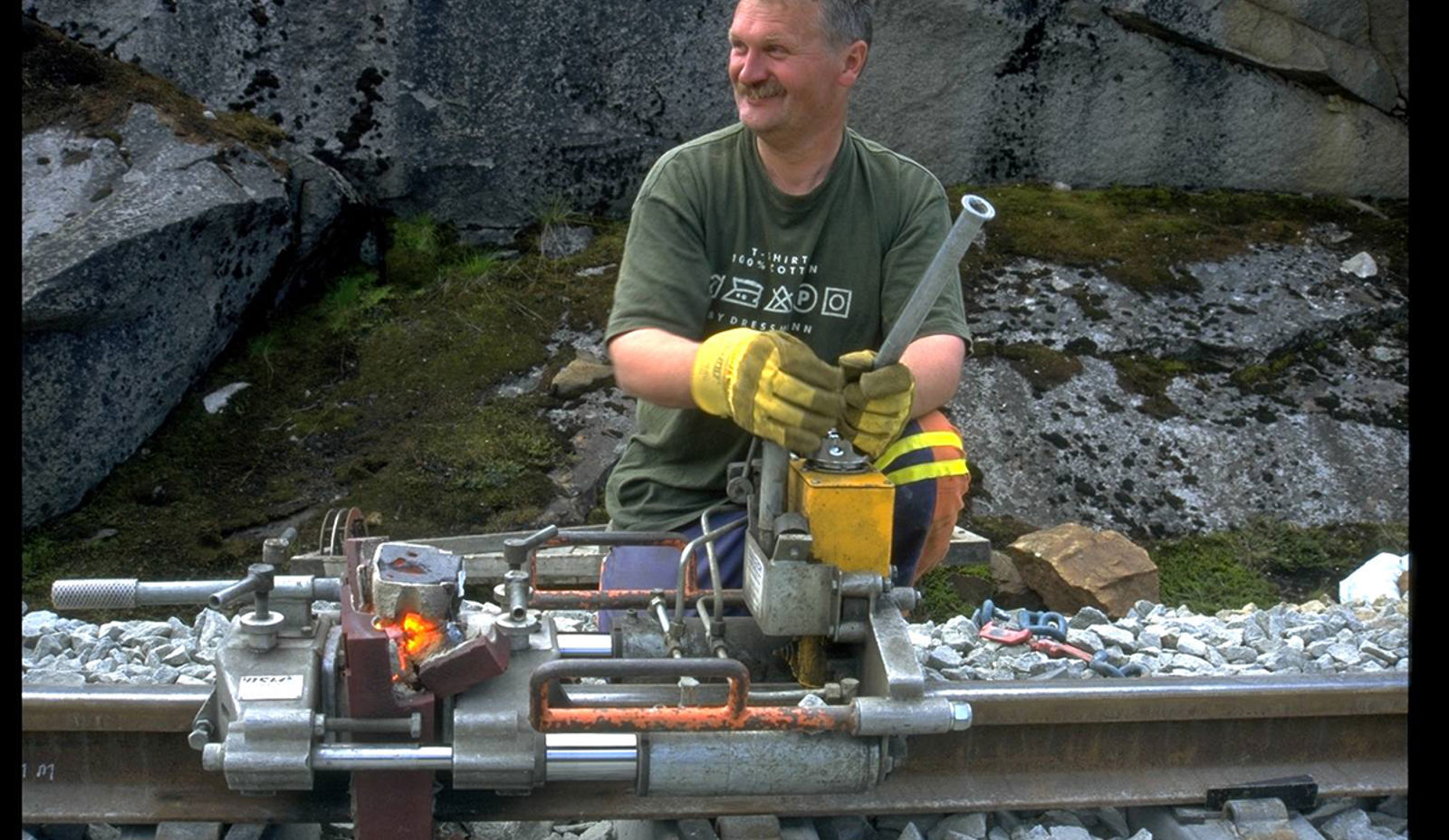 Jernbanearbeider bruker hydraulisk apparat for å skjære bort sveisevulsten på skinnehodet.