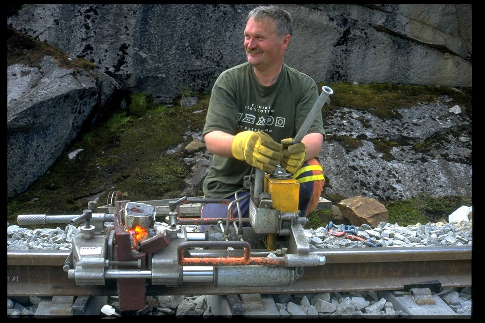 Jernbanearbeider bruker hydraulisk apparat for å skjære bort sveisevulsten på skinnehodet.