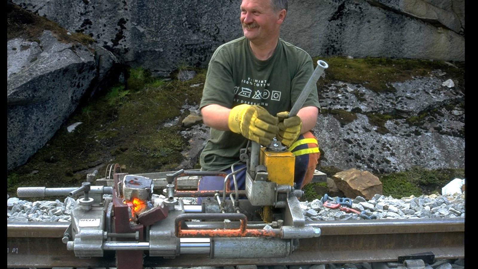 Jernbanearbeider bruker hydraulisk apparat for å skjære bort sveisevulsten på skinnehodet.
