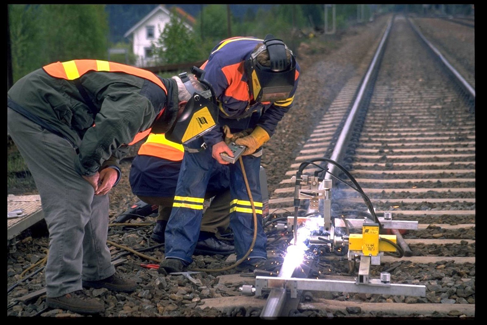 Arbeidere utfører påleggsveising av skinne med sveiseautomat.