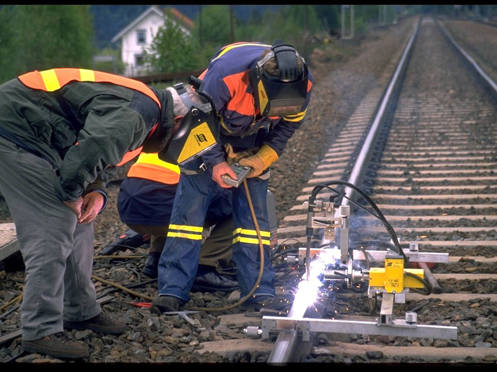 Arbeidere utfører påleggsveising av skinne med sveiseautomat.