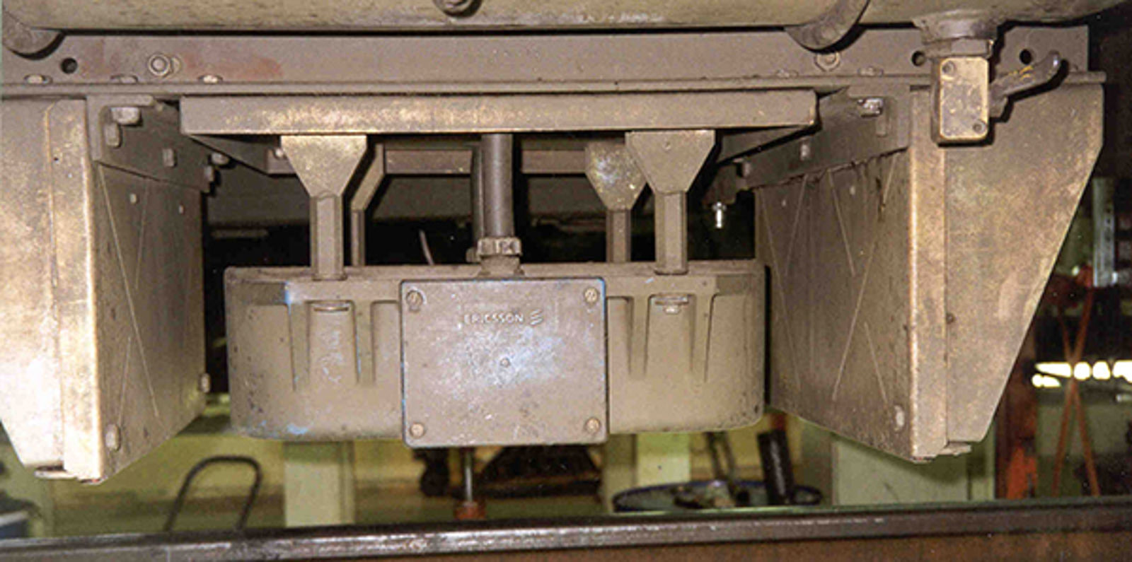 Gammel type ATC-antenne med metallbeskyttelse foran og bak, montert under lokomotiv.